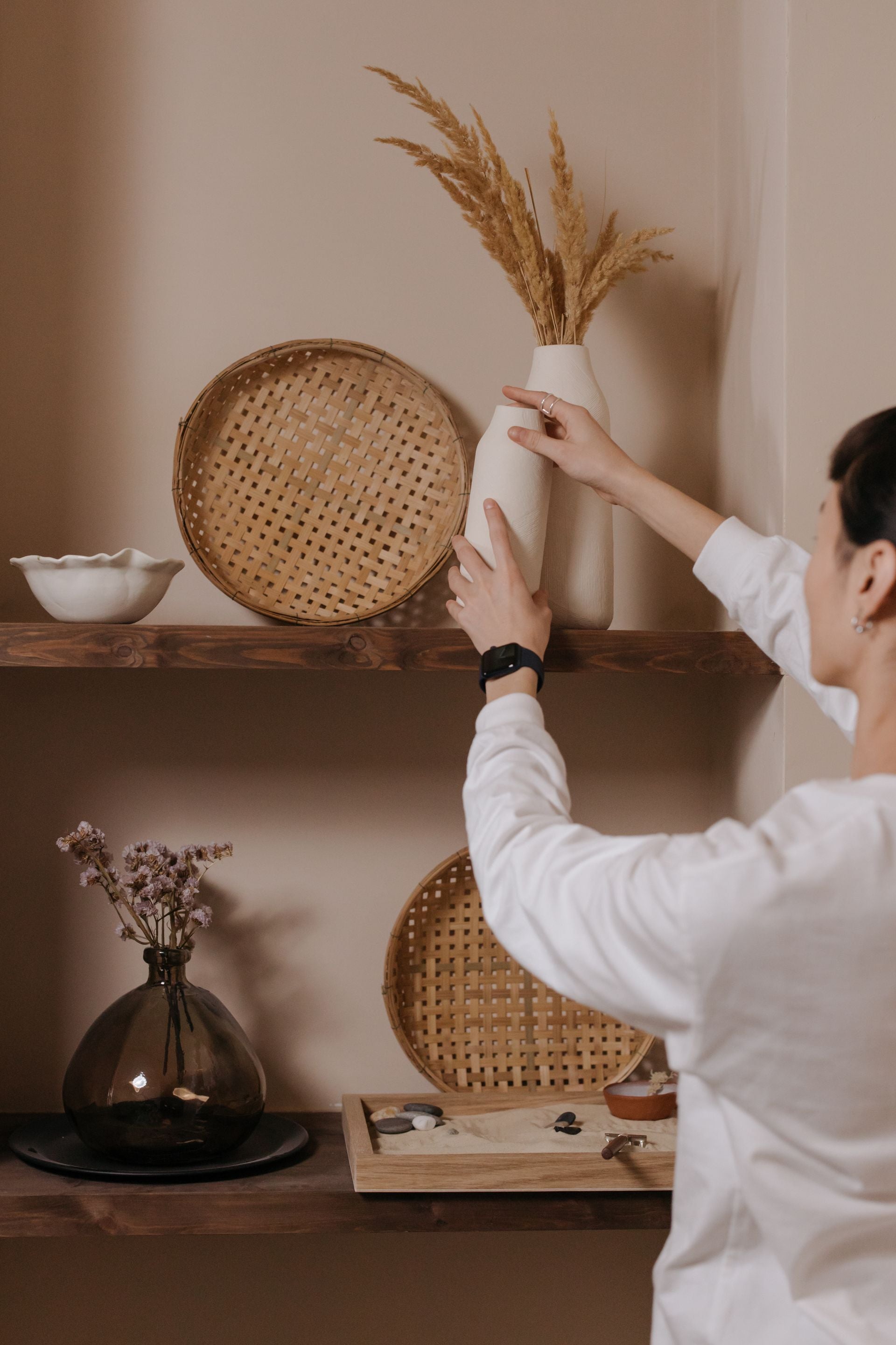 Person arranging decorative items on a shelf with a neutral background