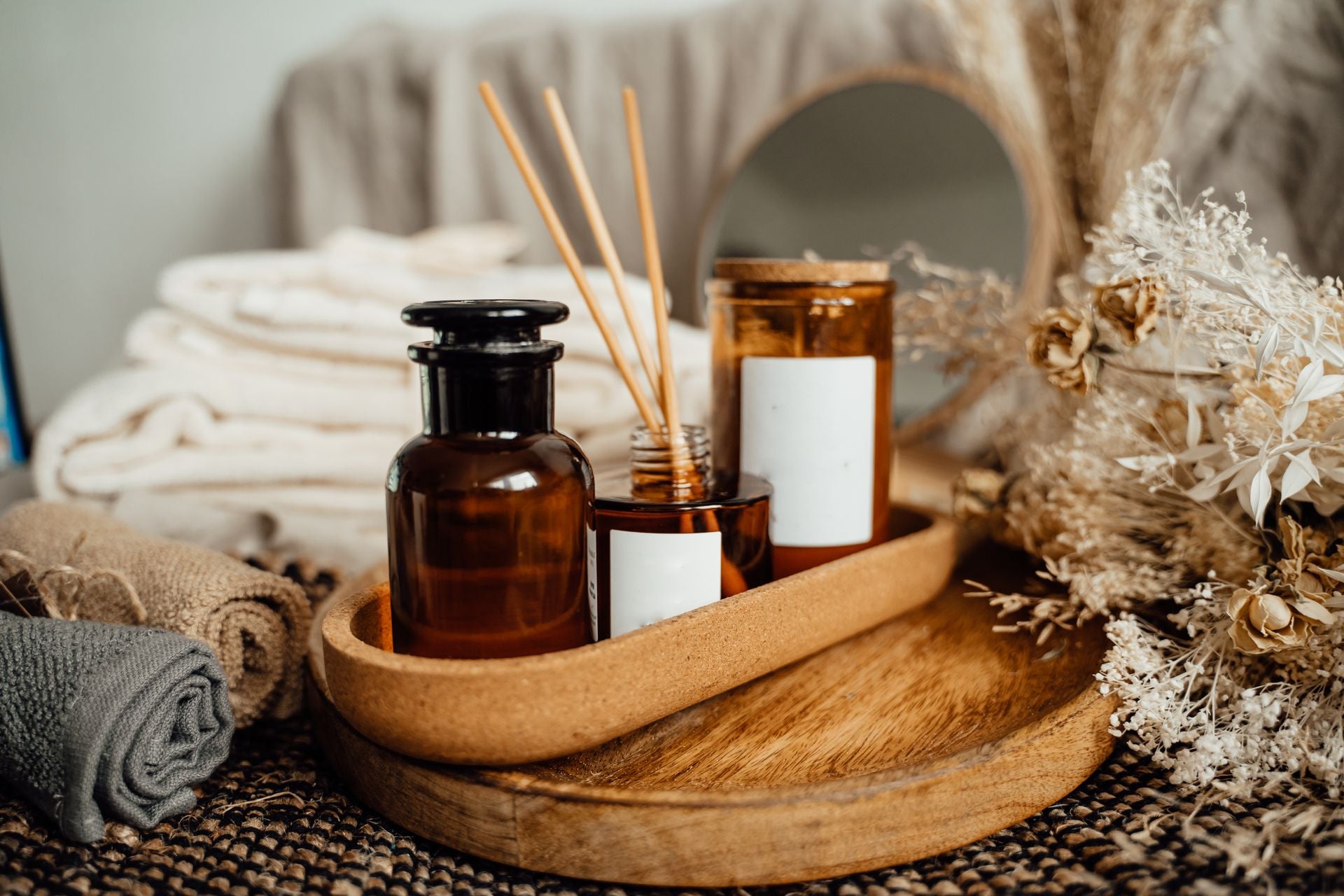 A wooden tray with brown bottles, a candle, and rolled towels on a textured surface.
